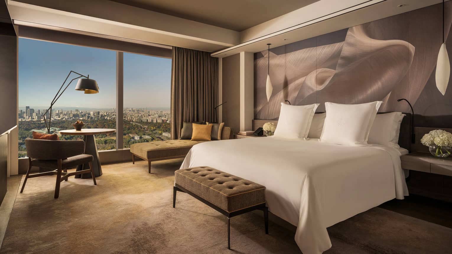 Hotel room with a cushioned bench at the end of white king bed and a wall of windows