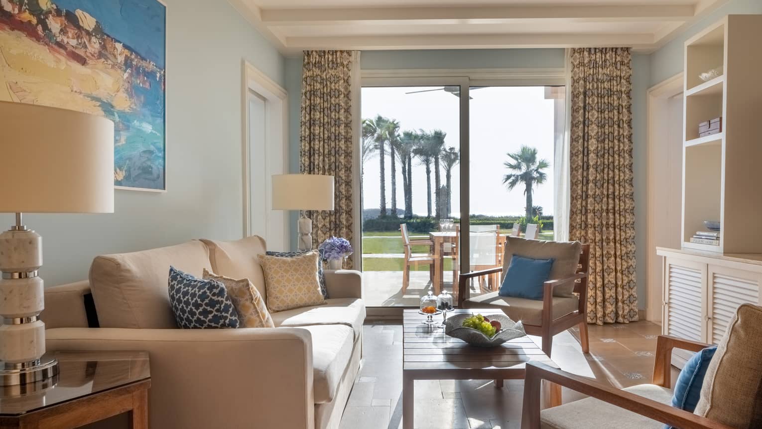 Guest room living area with tan sofa and armchairs, coffee table, sliding glass door to patio