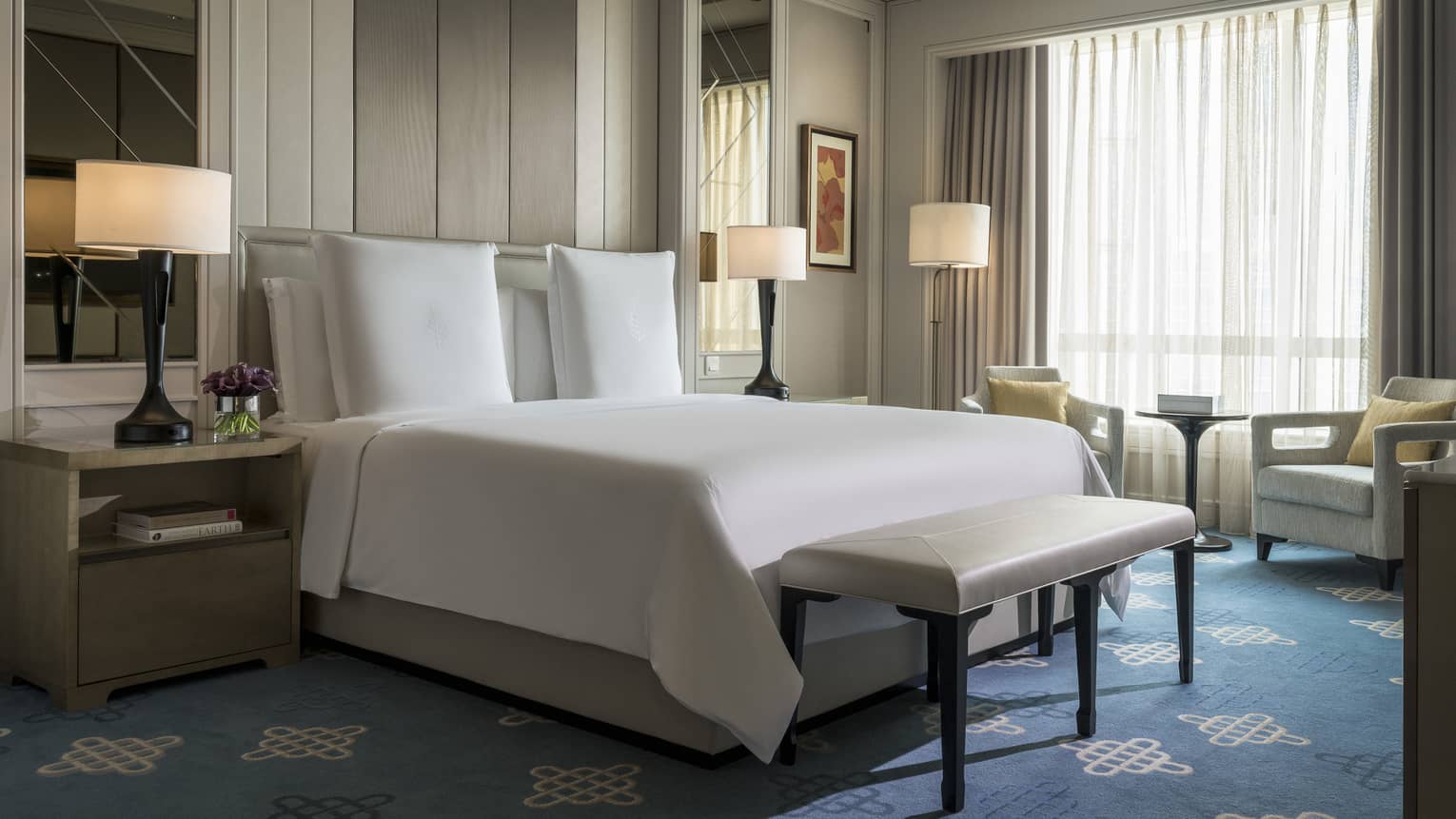 Superior Room mirrors, lamps on sides of hotel bed, bench at foot, armchairs at window