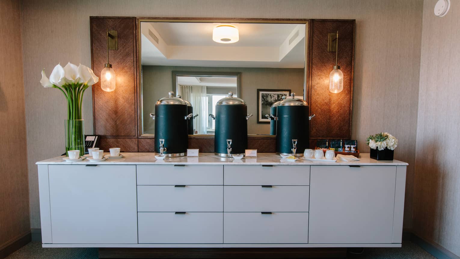 A white dresser with pitchers and flowers on top.
