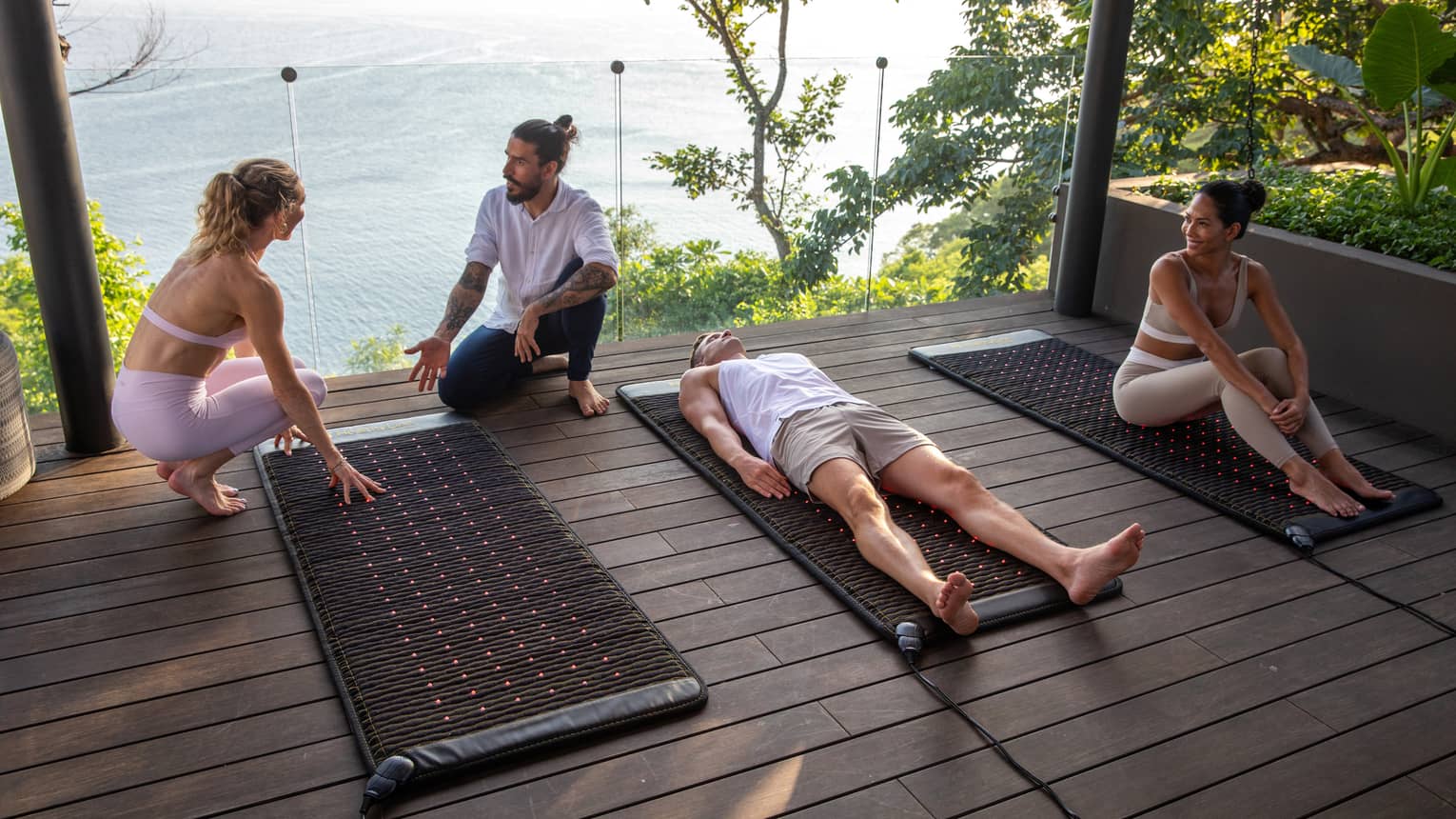 Three people sit and lay on red-light therapy mats as an instructor talks