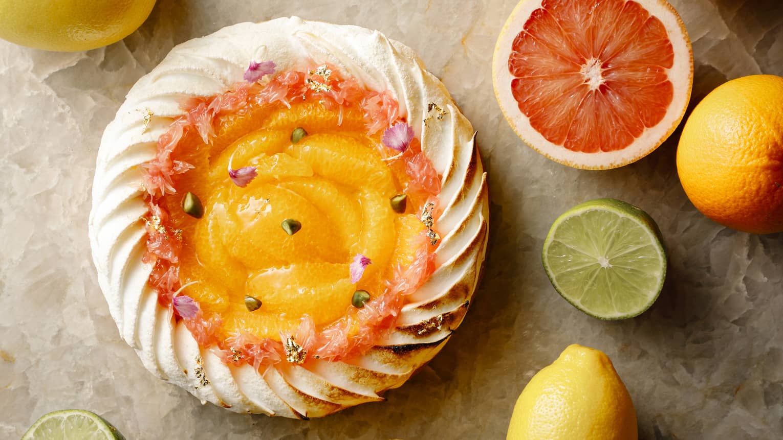Aerial shot of whole citrus tart rimmed with pastry cream, halved citrus fruit on table surrounding it