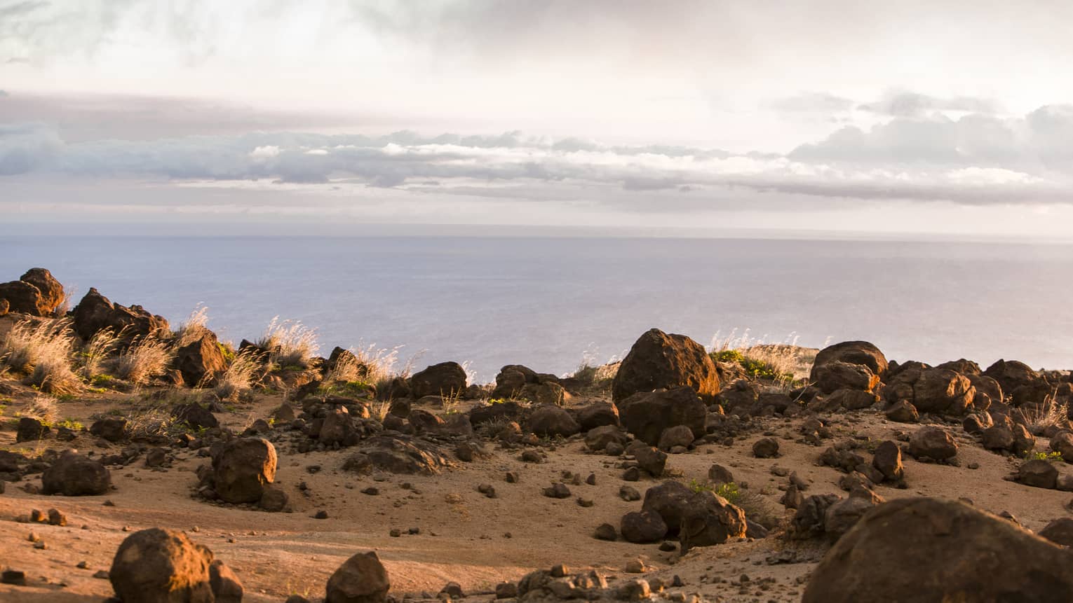 Rocky cliffside at sunset overlooking the ocean, wispy white clouds above