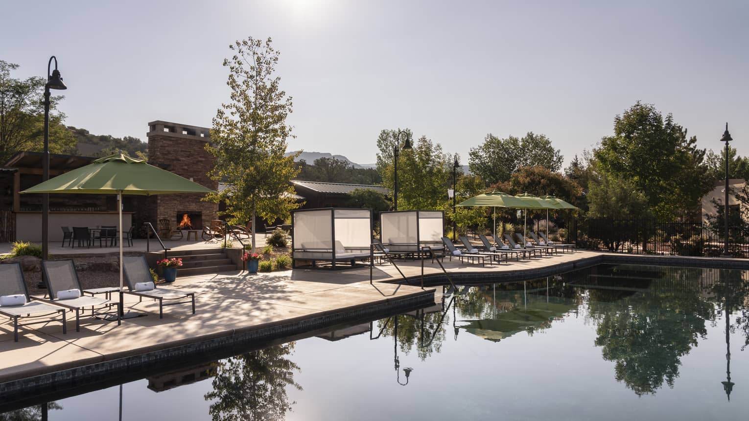 An outdoor pool near trees, lounge chairs, and green umbrellas.