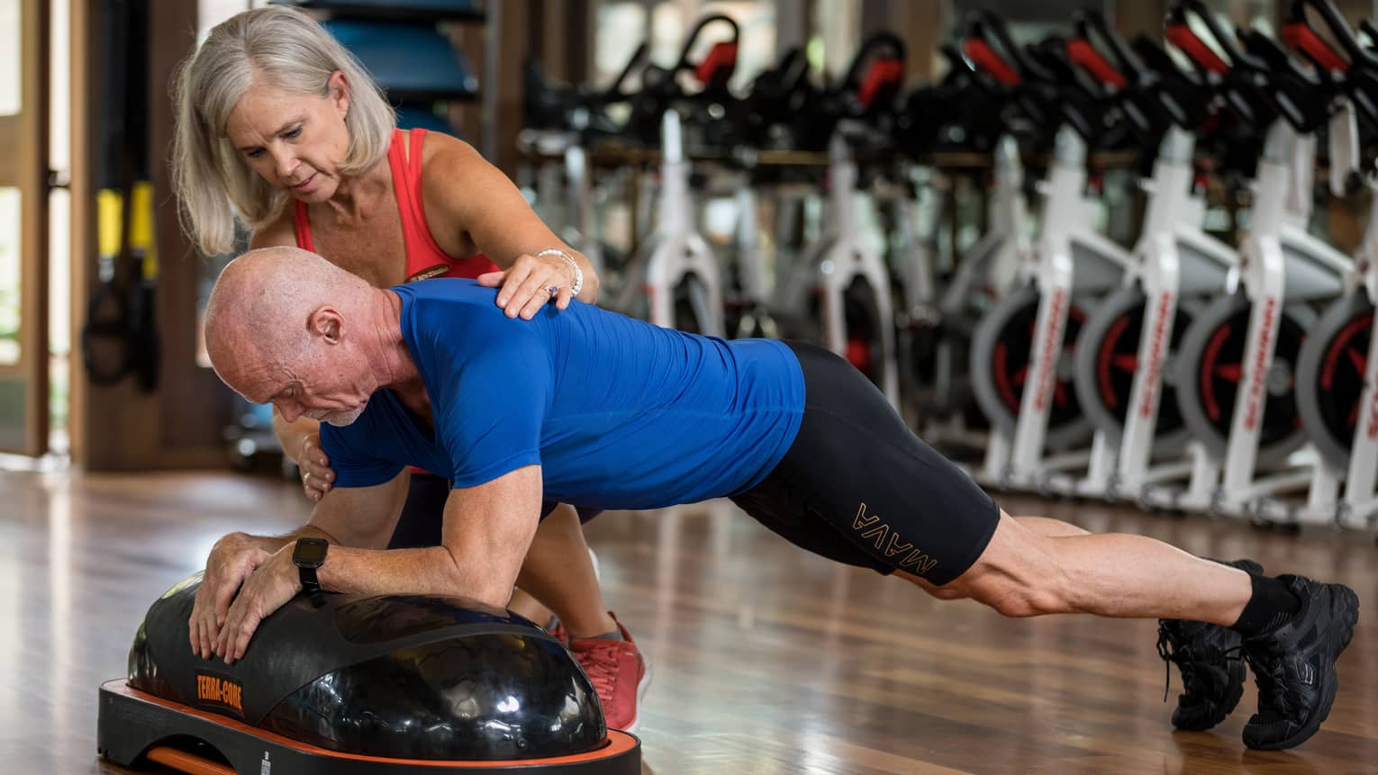 Fitness trainer helps man balance on pilates board in exercise studio