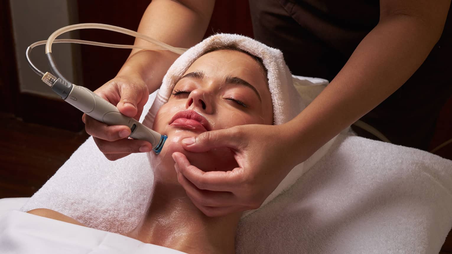 Spa therapist performs facial on female guest with tool