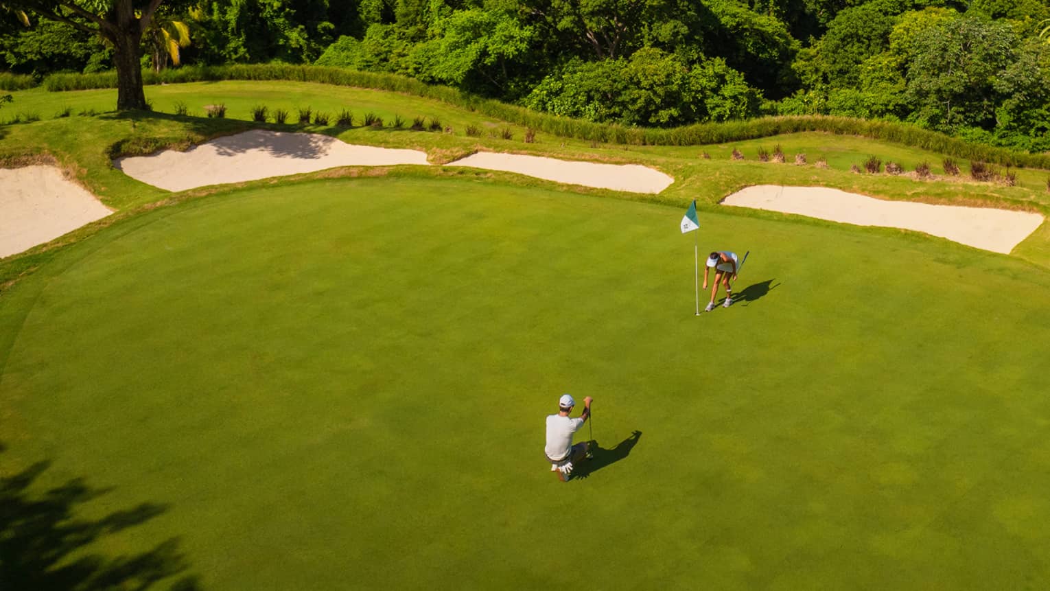 Aerial view of two golfers on a green with the ocean in the background