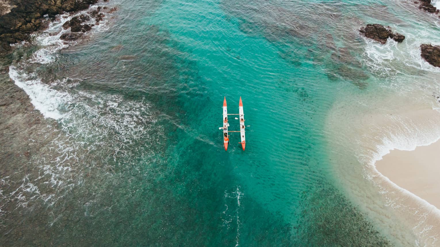 Two sea kayaks make their way through blue-green water along a rocky coastline