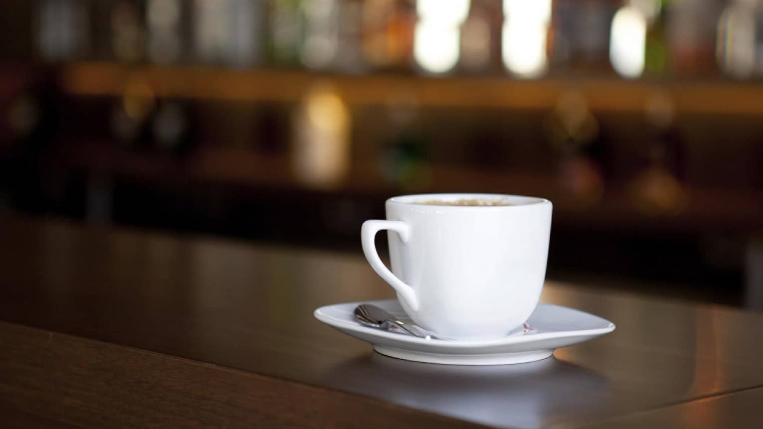 A white coffee cup and matching saucer, sitting on a dark wooden bar