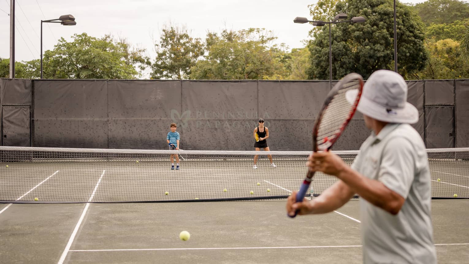 A man, woman and young boy holding racquets on a tennis court
