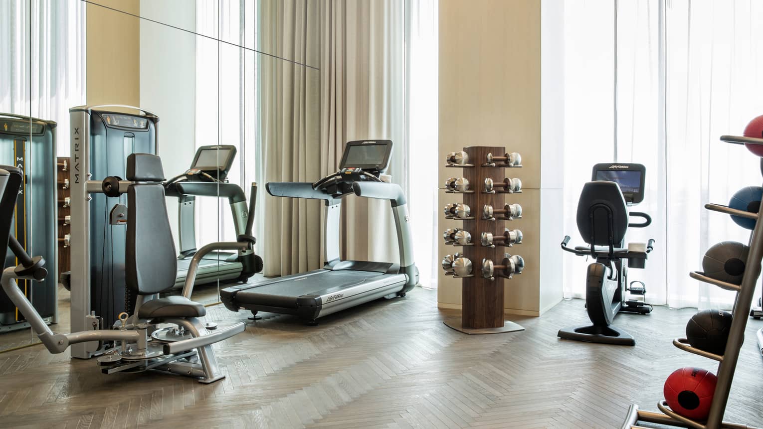 Cardio exercise machines, rack of hand weights near windows with long curtains in fitness centre