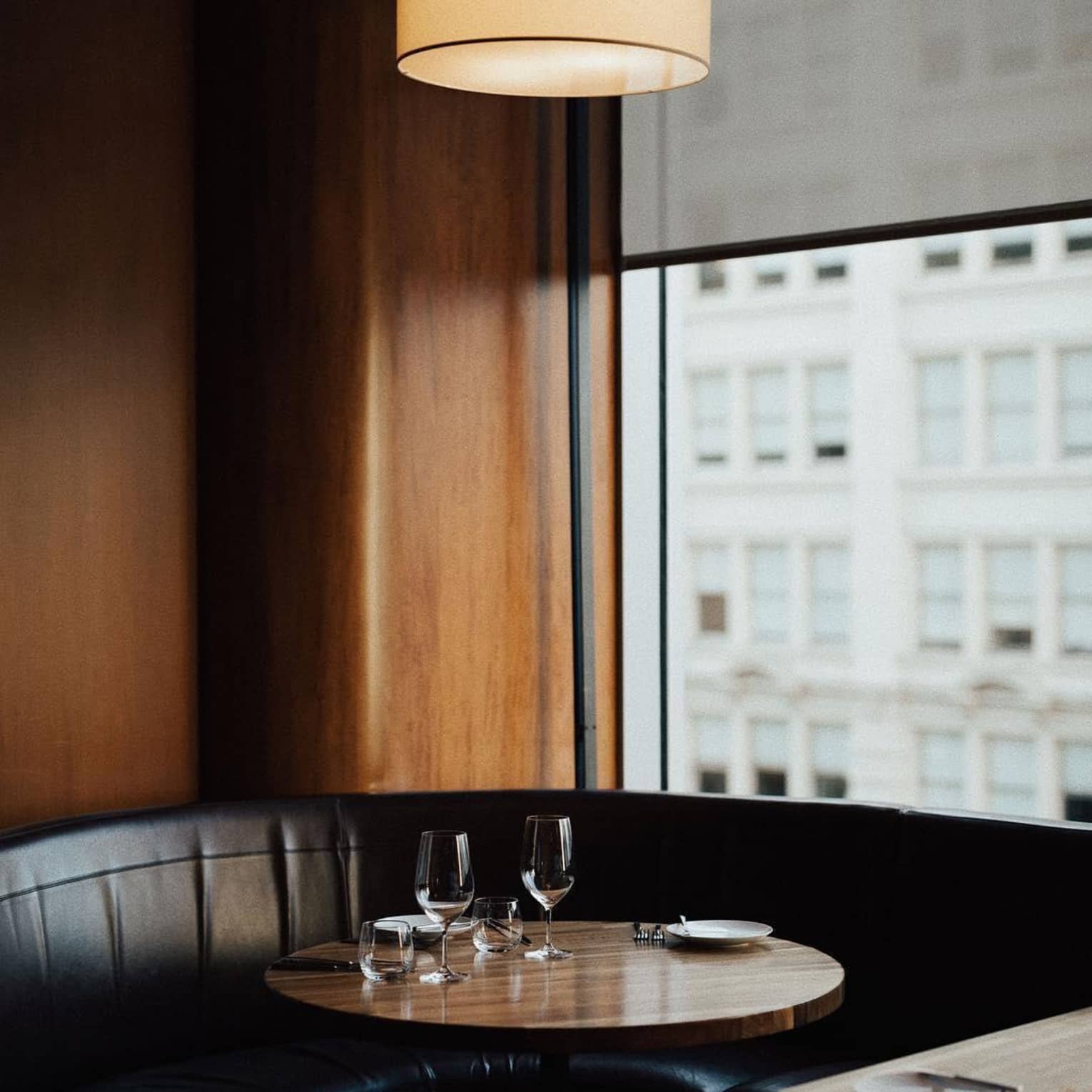 Round light over black leather banquette dining table, dark wood wall and window