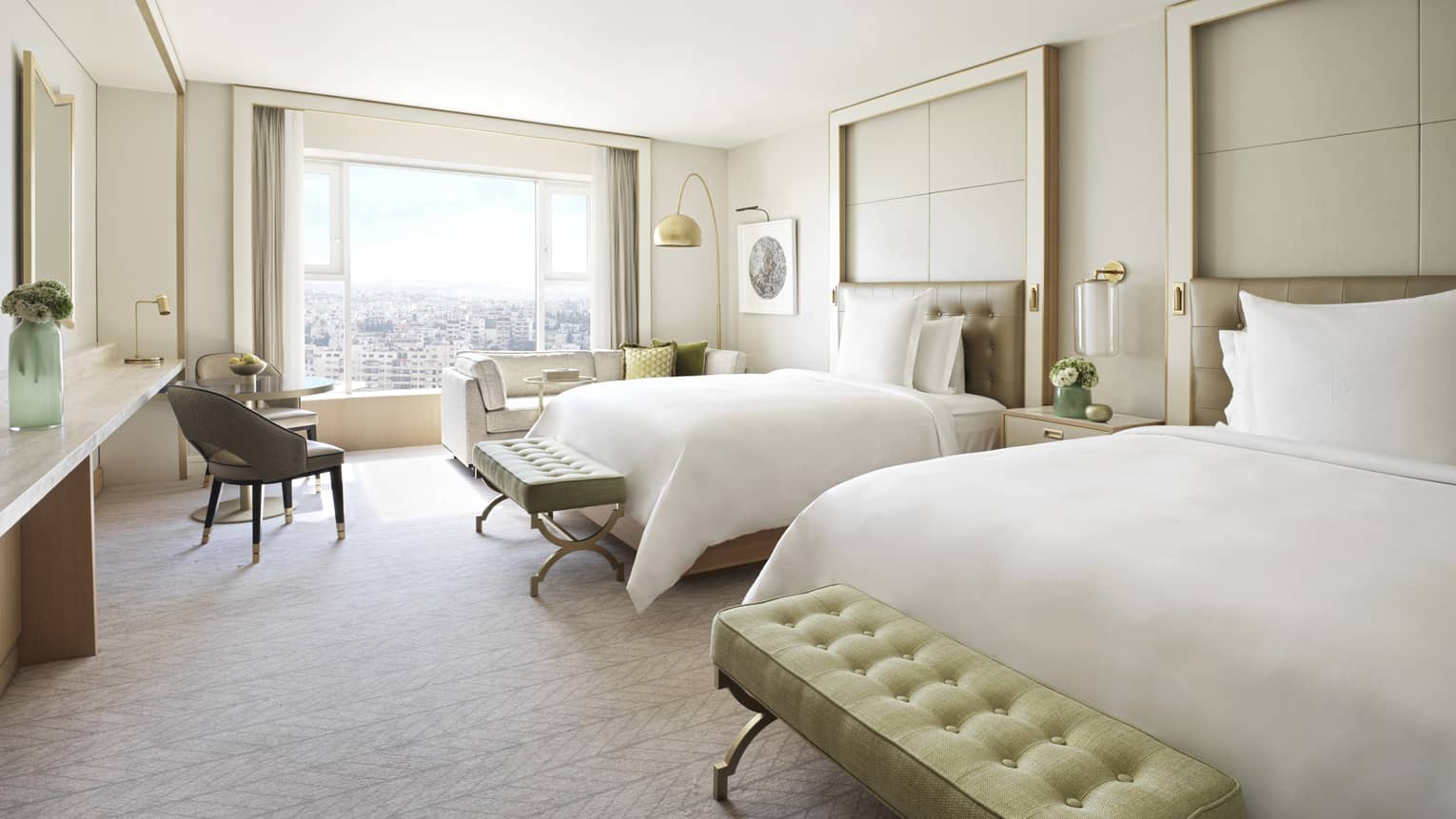 Bedroom with two plush twin beds, each with light green ottoman. Large window and arm chair.