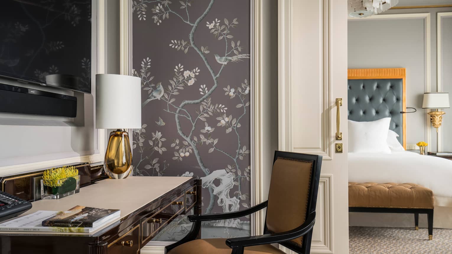 Black desk with orange glass lamp with white shade, wall panel with lilac tone images of trees, birds