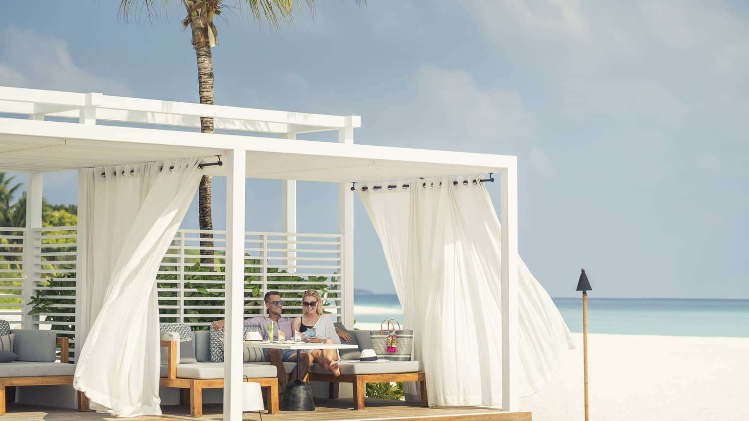 Guests enjoying cocktails and a slight breeze next to the water at a Blu Beach Club Cabana