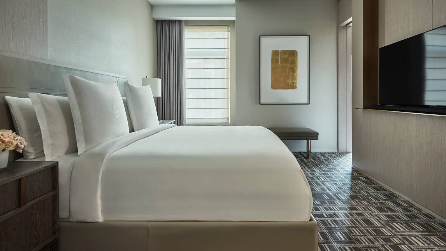 Hudson Suite side view of bed with white linens across from TV, black-and-white carpet