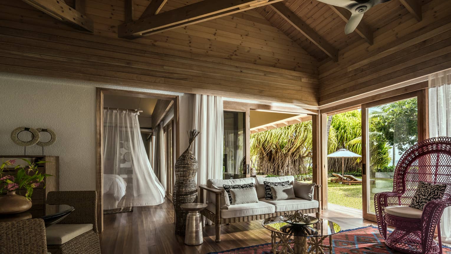 One-bedroom suite living room wicker furniture under wood beam roof, bed with white sheer canopy