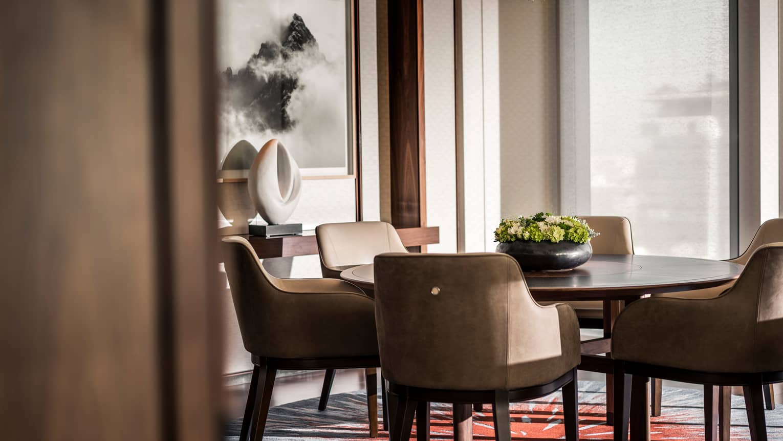 Leather dining chairs around round table with flowers, console table with white sculpture under painting