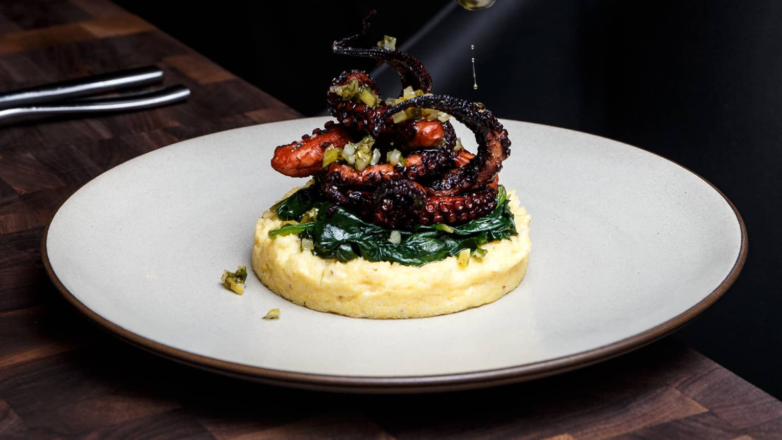 Detail of chef putting garnish on plate of grilled octopus and polenta