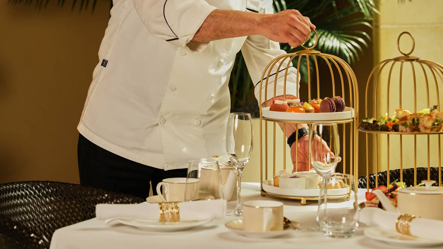 Chef places a tiered tray of pastries onto a table set for afternoon tea