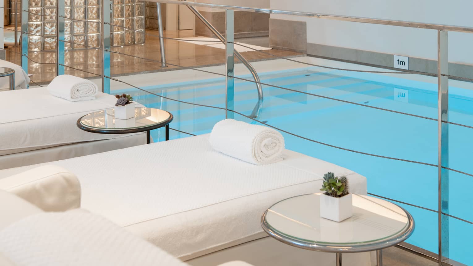 A spacious, well-lit indoor pool area with comfortable poolside spa treatment tables