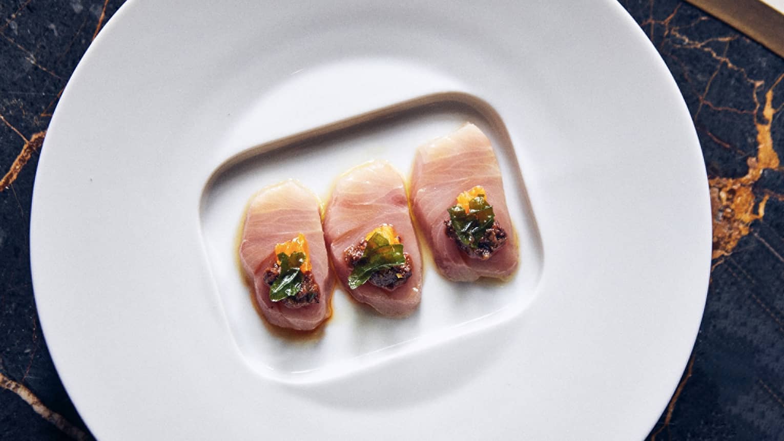 Raw fish slices with herbs on a white plate.