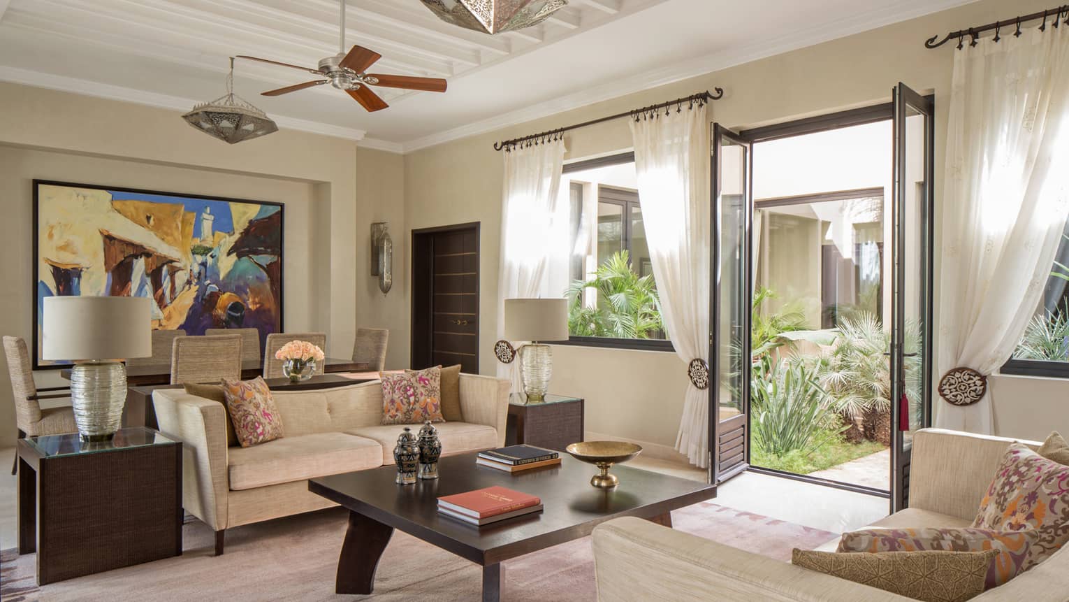 Two Bedroom Villa living room with two sofas around large coffee table with books, dining table, large colourful painting