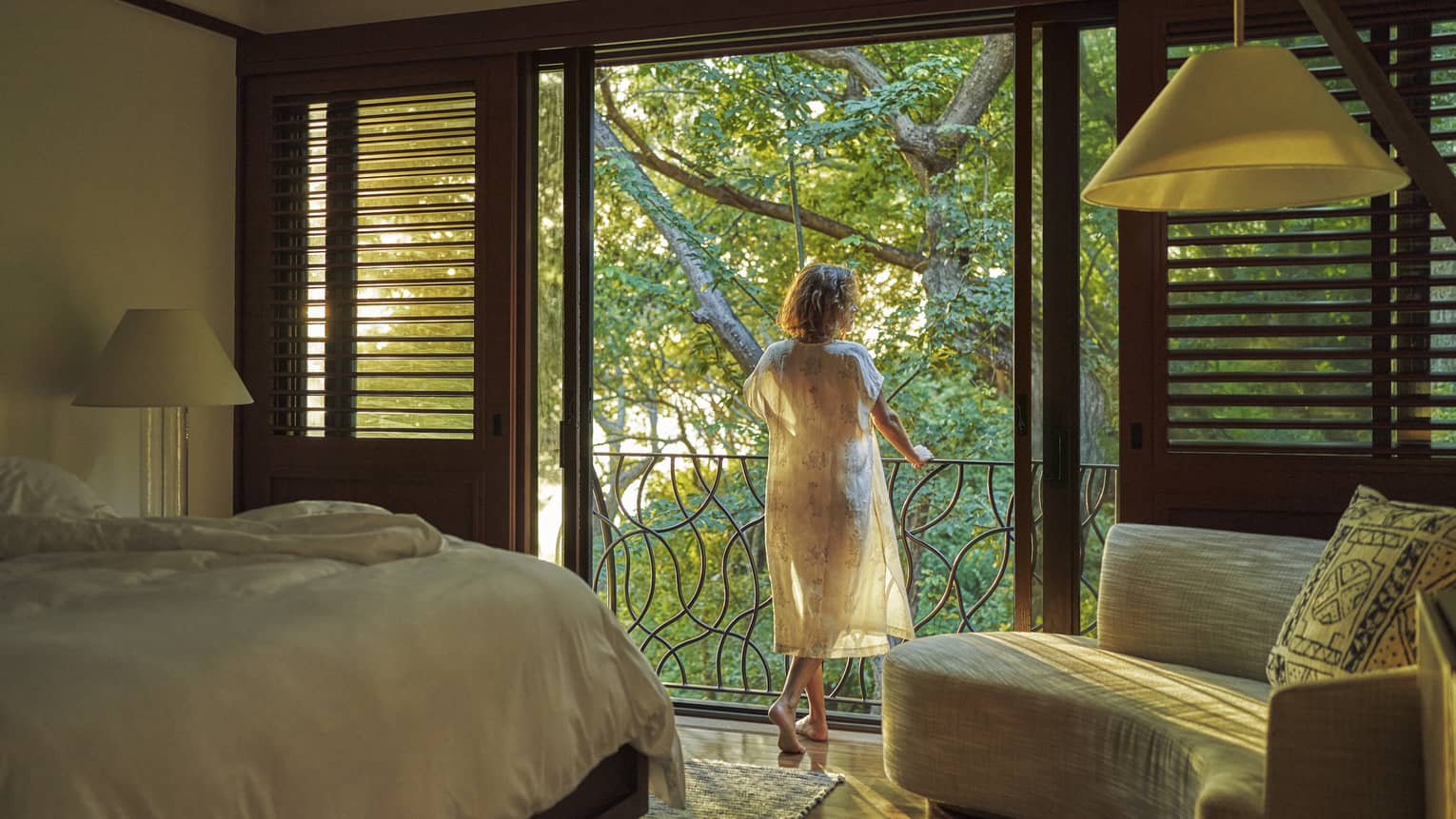Woman stands at balcony from bedroom, looking out to jungle