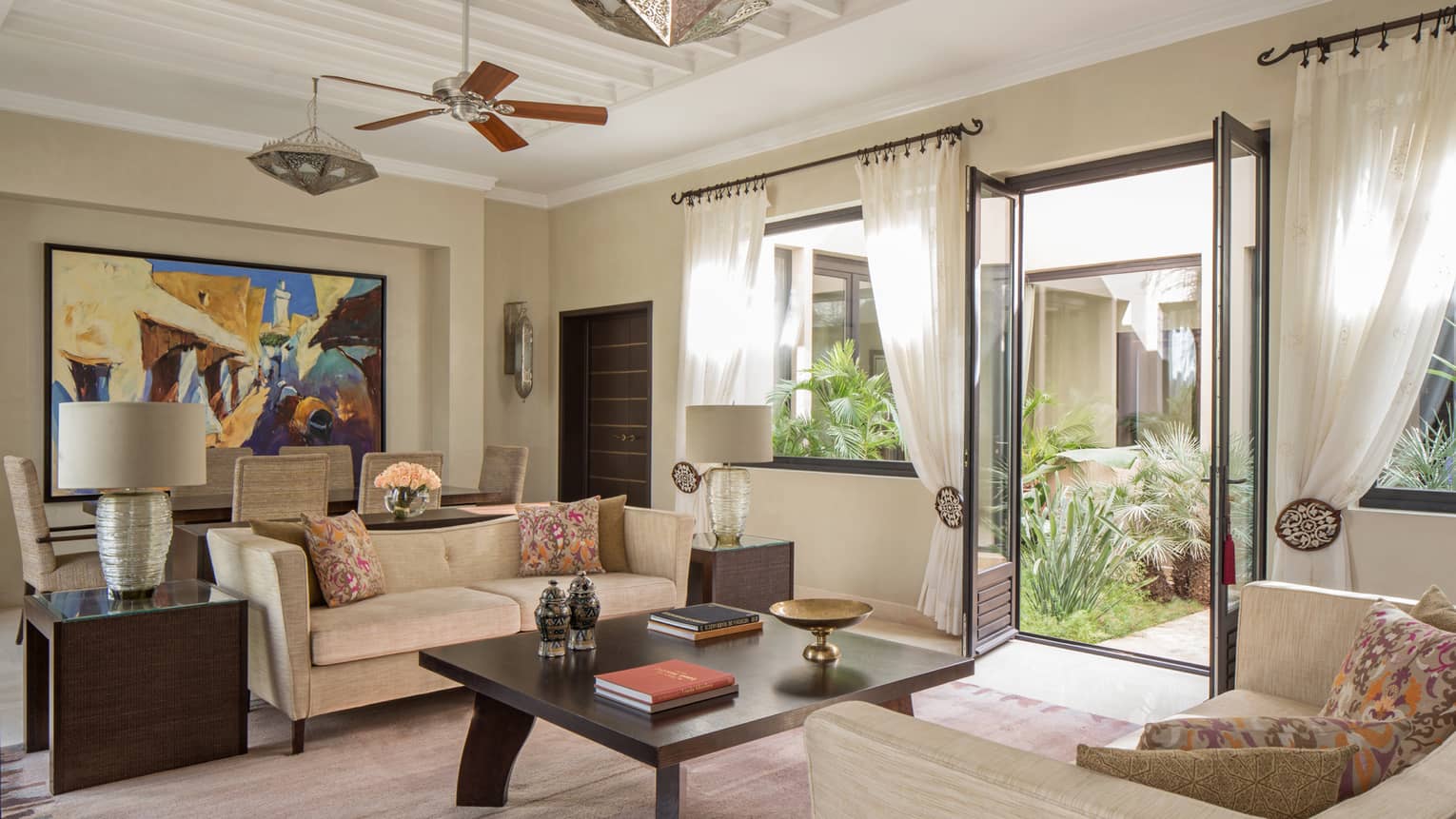 Two Bedroom Villa living room with two sofas around large coffee table with books, dining table, large colourful painting