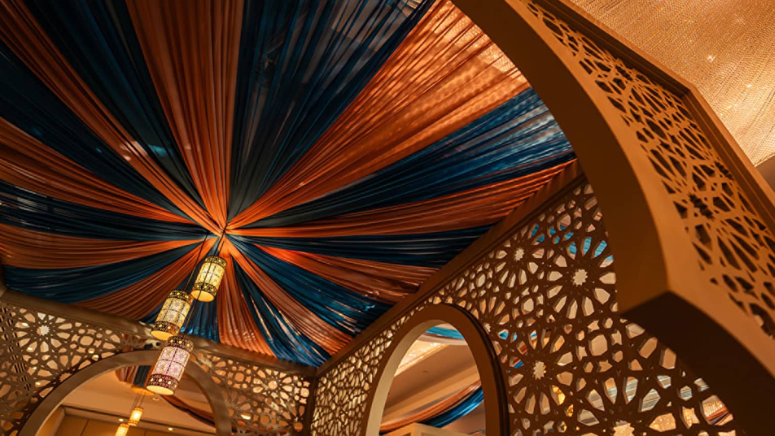 Ceiling draped in alternating brown and blue fabric panels with arabesque-style lanterns hanging from the centre