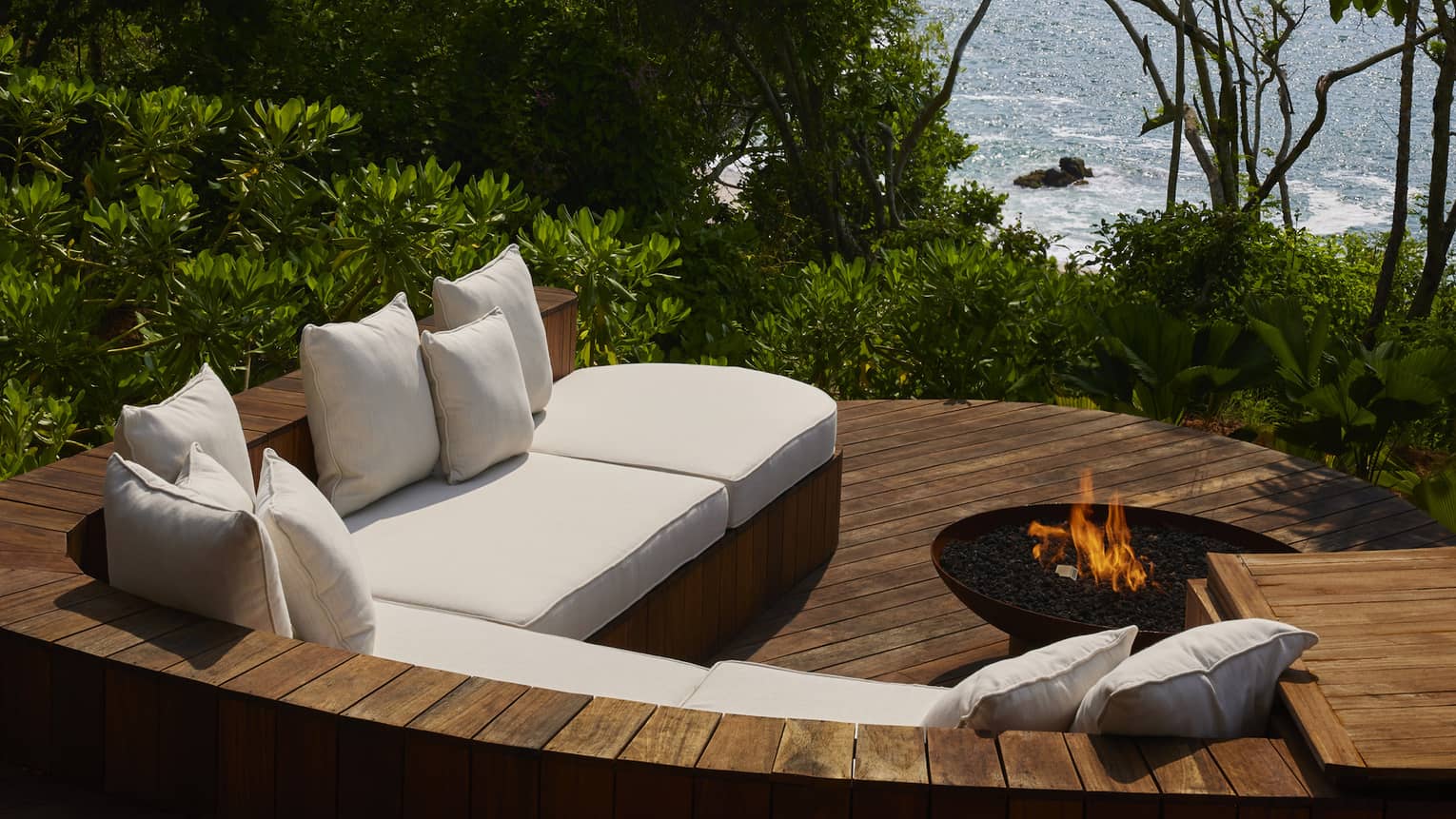 A sunken wooden patio with sofa and firepit, jungle and ocean view
