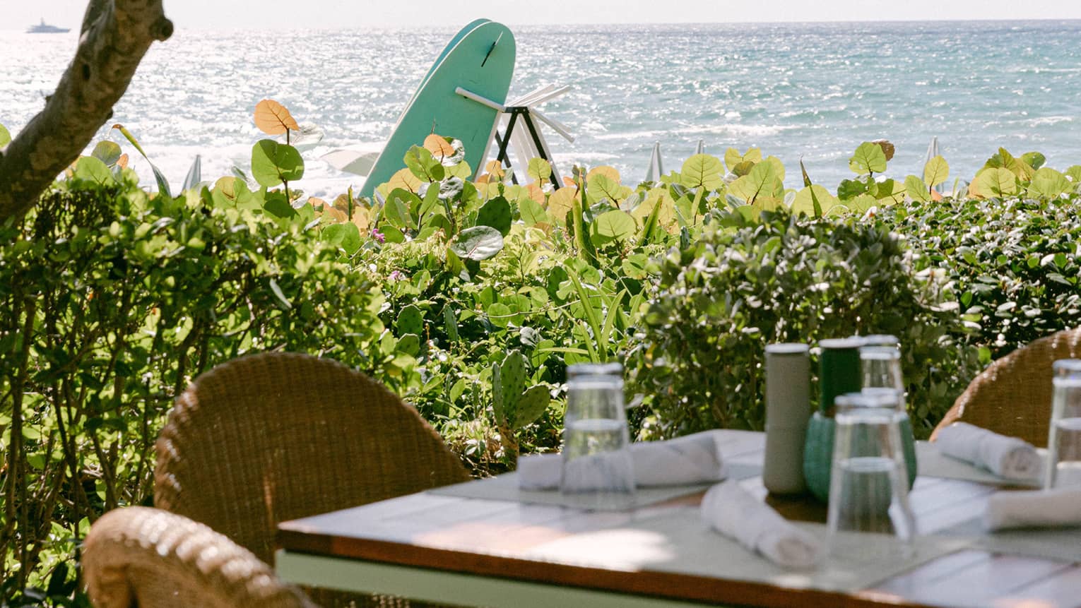 Outdoor dining table set beneath a green-and-white umbrella overlooking the ocean