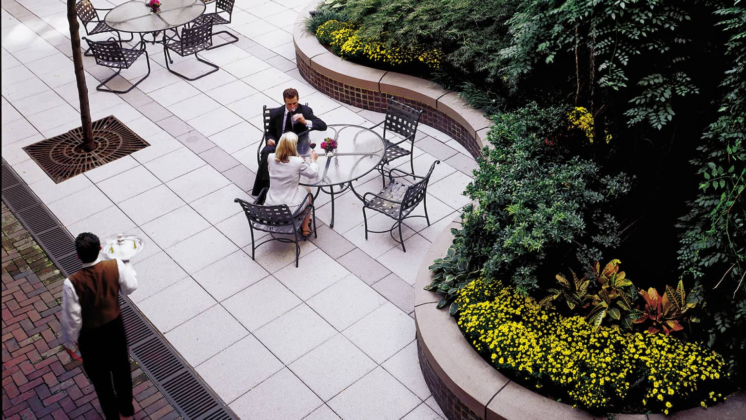 Aerial view of people at patio table in hotel courtyard, curved path and large garden bed