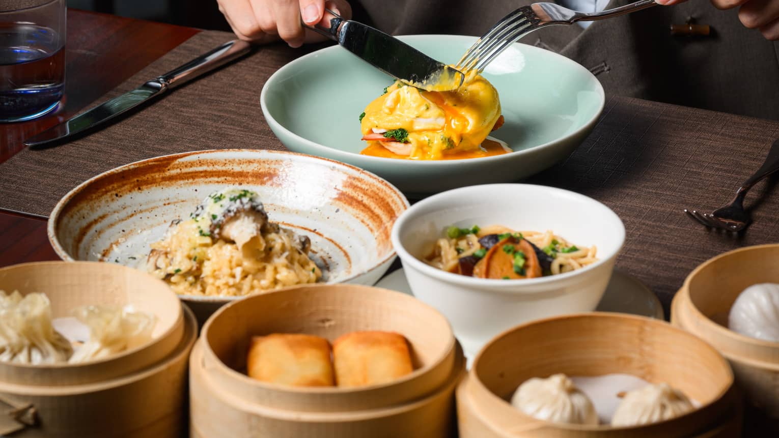A guest enjoying an egg sandwich, with a mushroom risotto, a noodle dish and a medley of dim sum also laid out on the table.