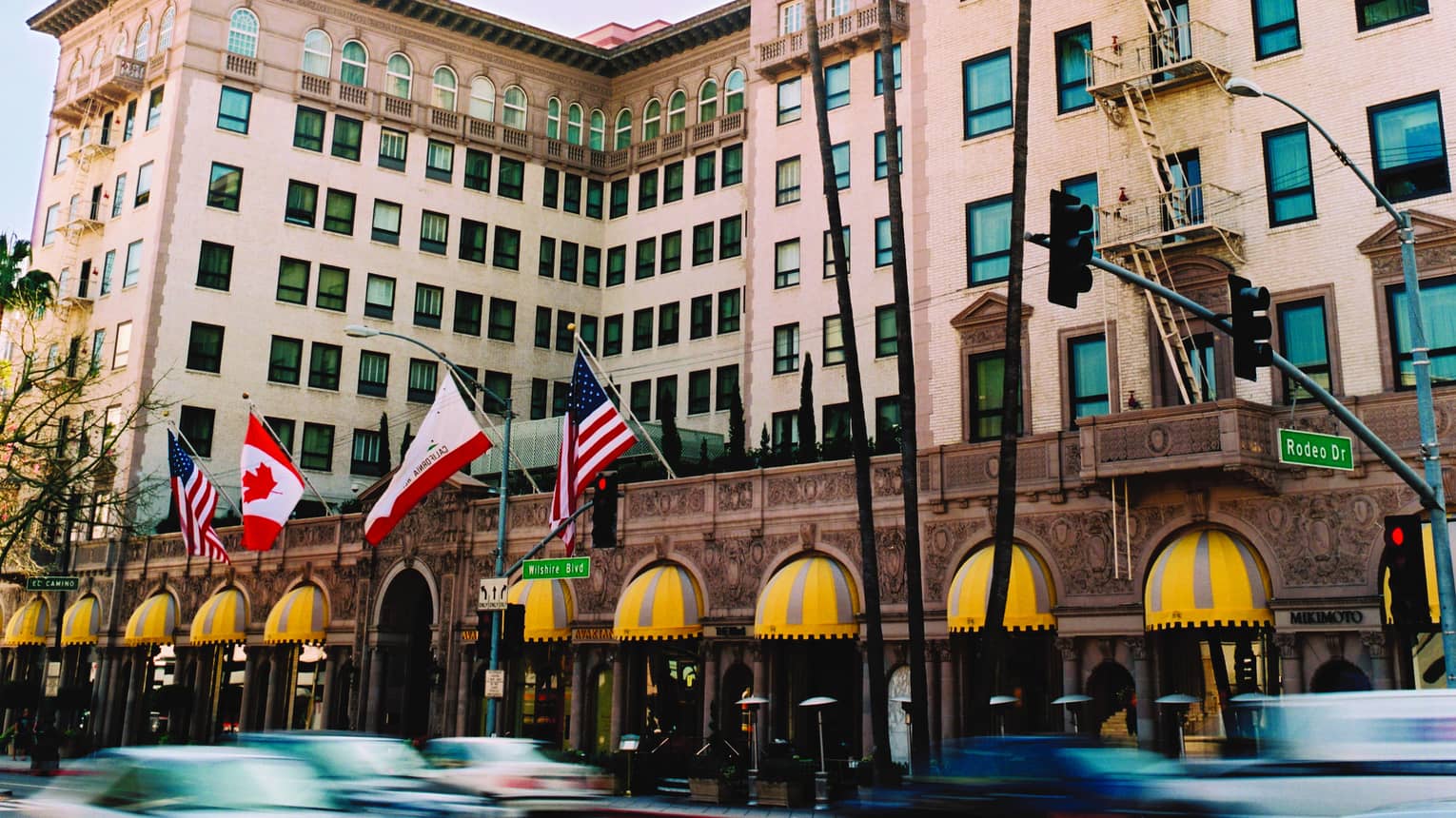 Car drive by the pink four seasons Beverly Wilshire as flags fly in the wind and palm trees sway
