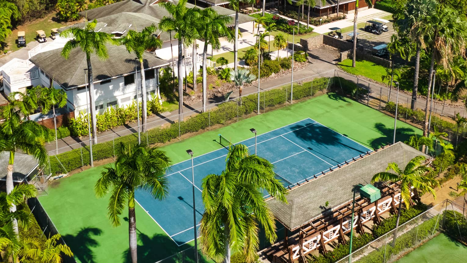 A tennis court surrounded by lush green trees, white building and a mountain in the background.