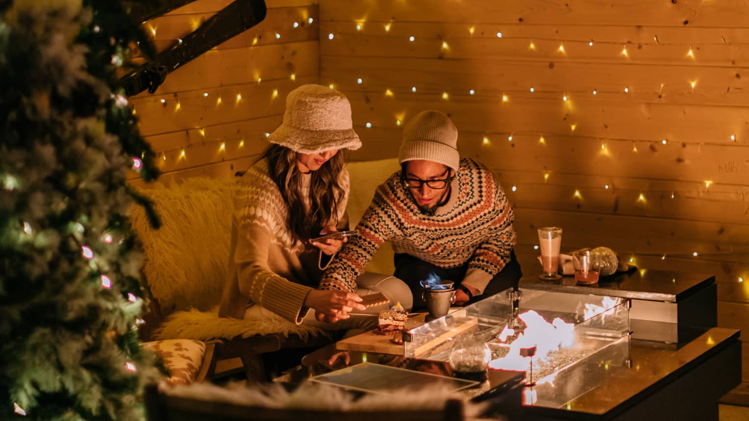 Two people sitting at a small table surrounded by plants and Christmas lights.