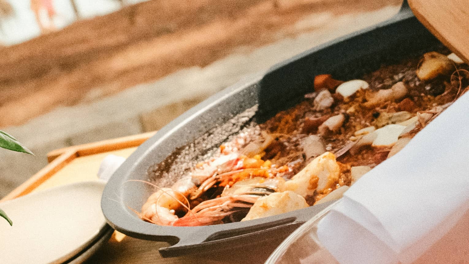 A person stirs a pan of cooked seafood with a wood spatula.
