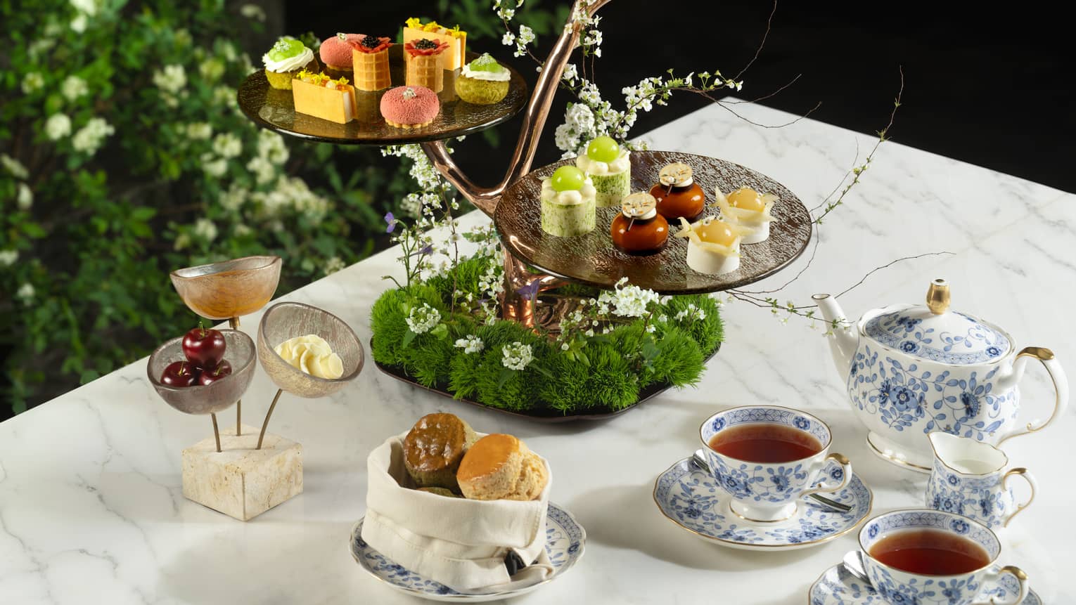 Tea and cakes on a table surrounded by greenery