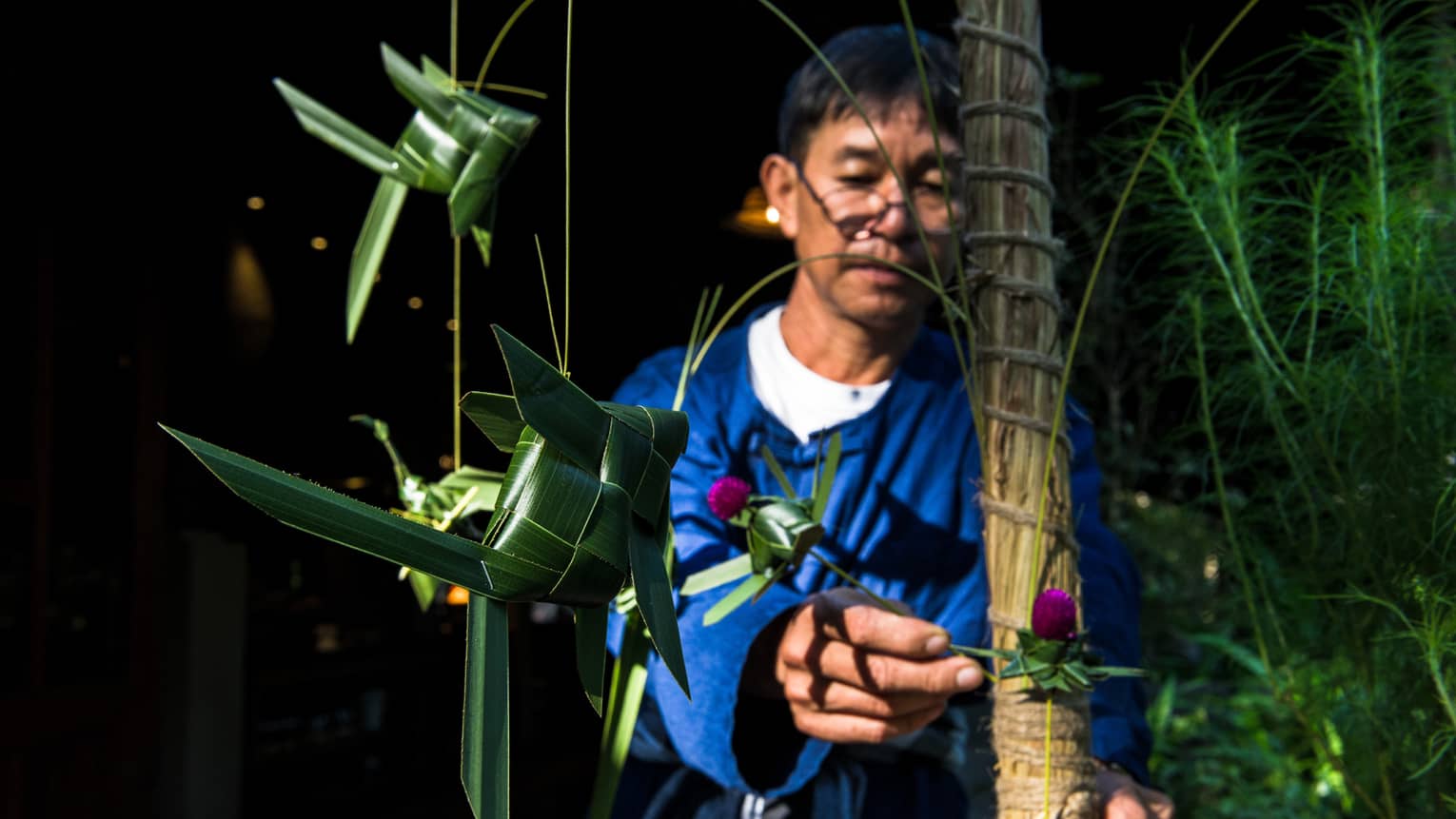 A man working with a tall tree amongst lush grass.