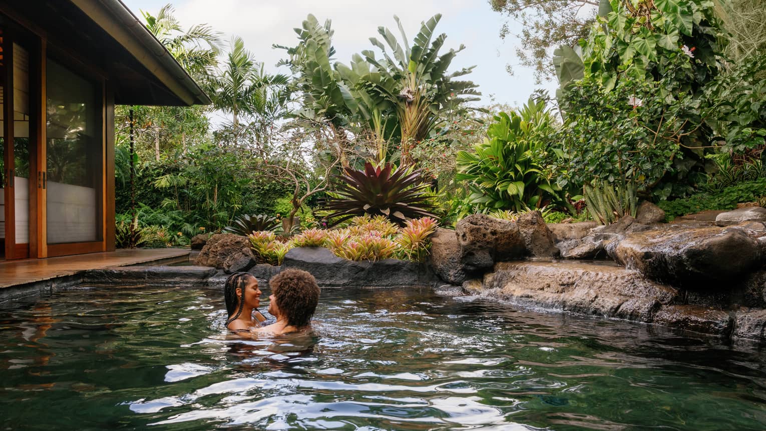 A man and woman embrace in a pond-like pool at a tropical resort
