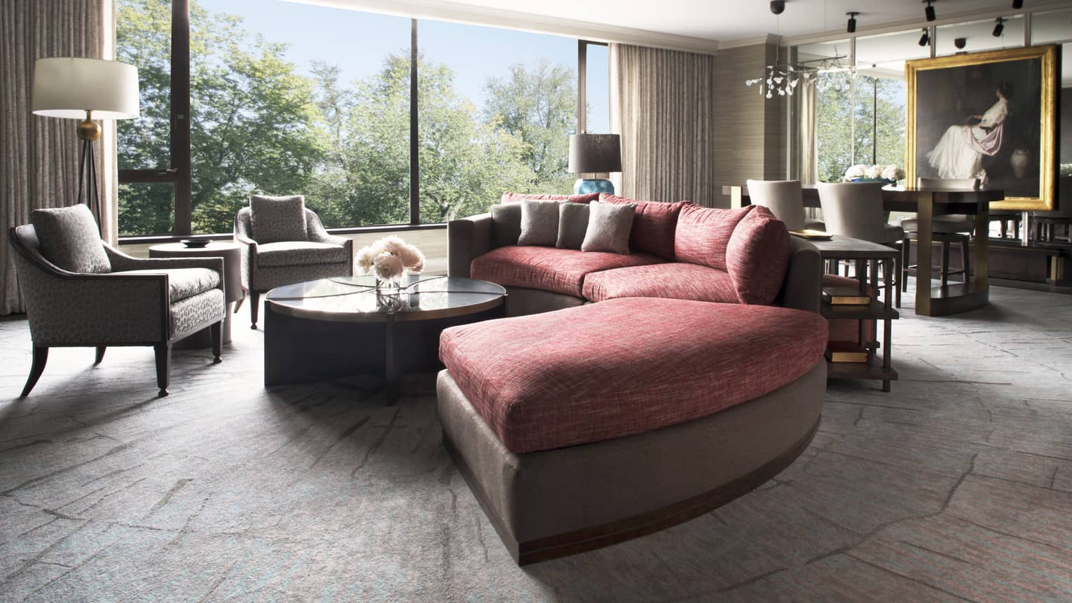 A large circular couch sits at the center of a well lit room, an intricate painting hangs in the background