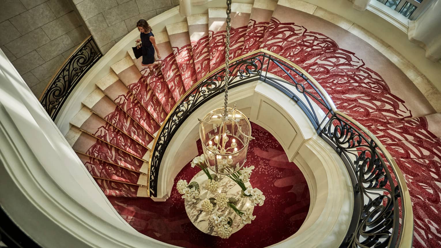 Aerial view of woman walking down white spiral staircase with red carpet, gold railing