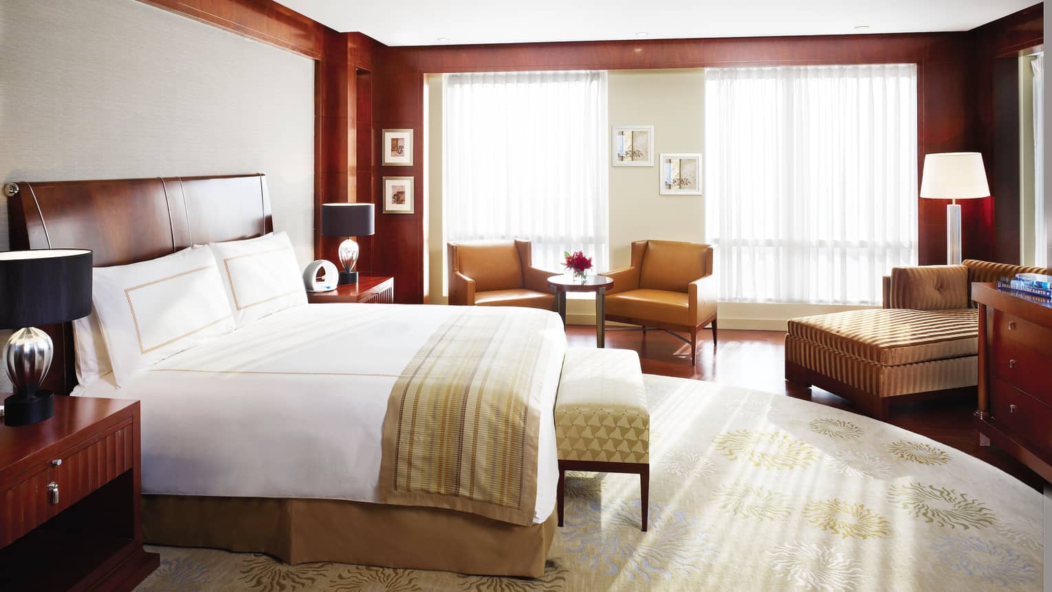 Presidential Suite bed, striped blanket, bench, brown leather armchairs and chaise by window