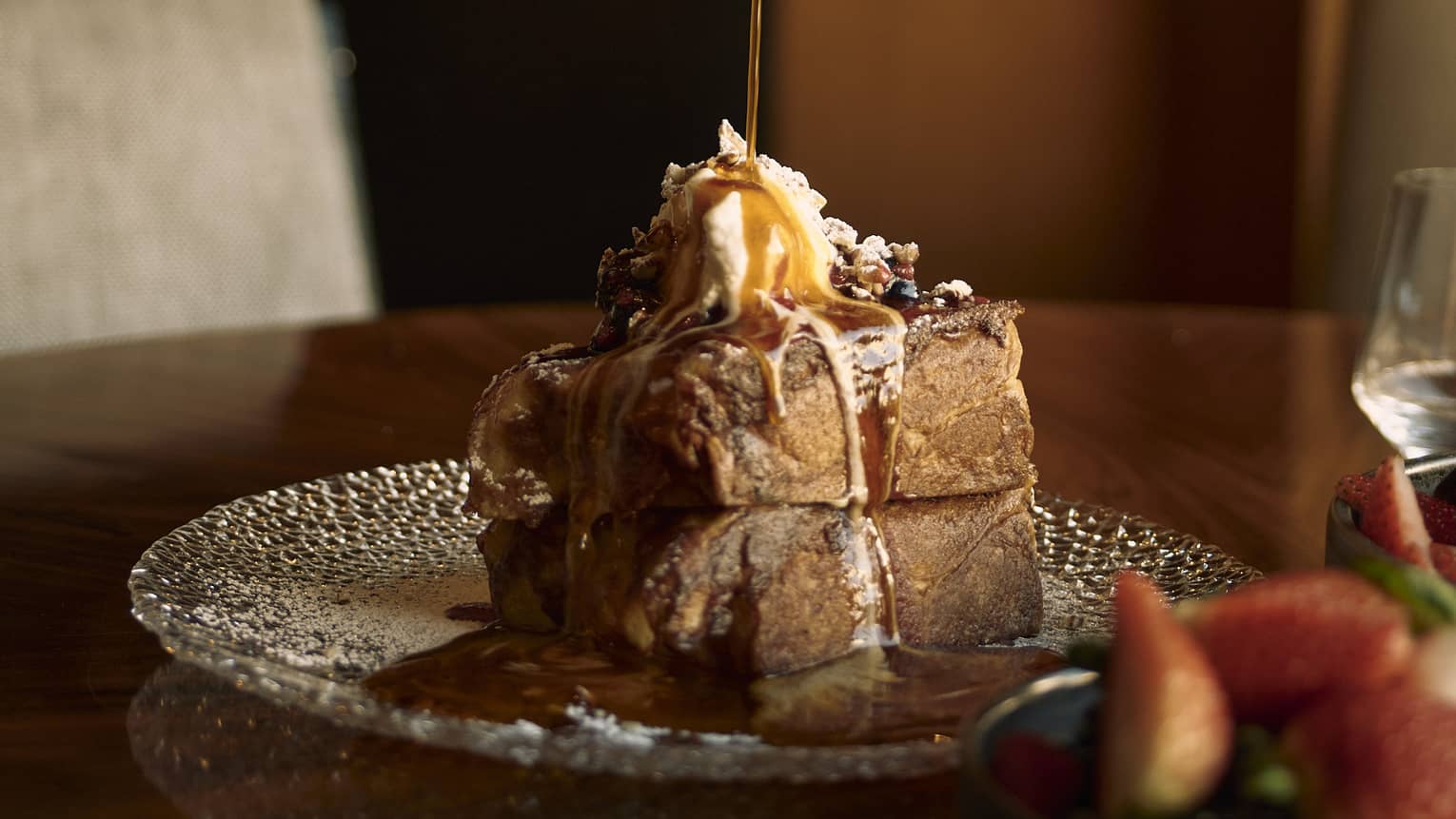 Person pouring maple syrup on two pieces of French toast with whipped cream