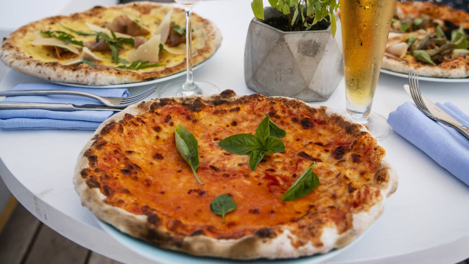 A table set with a glass of rose and a pilsner of beer with craft pizzas on it overlooking the beach at Four Seasons Maldives - Landa