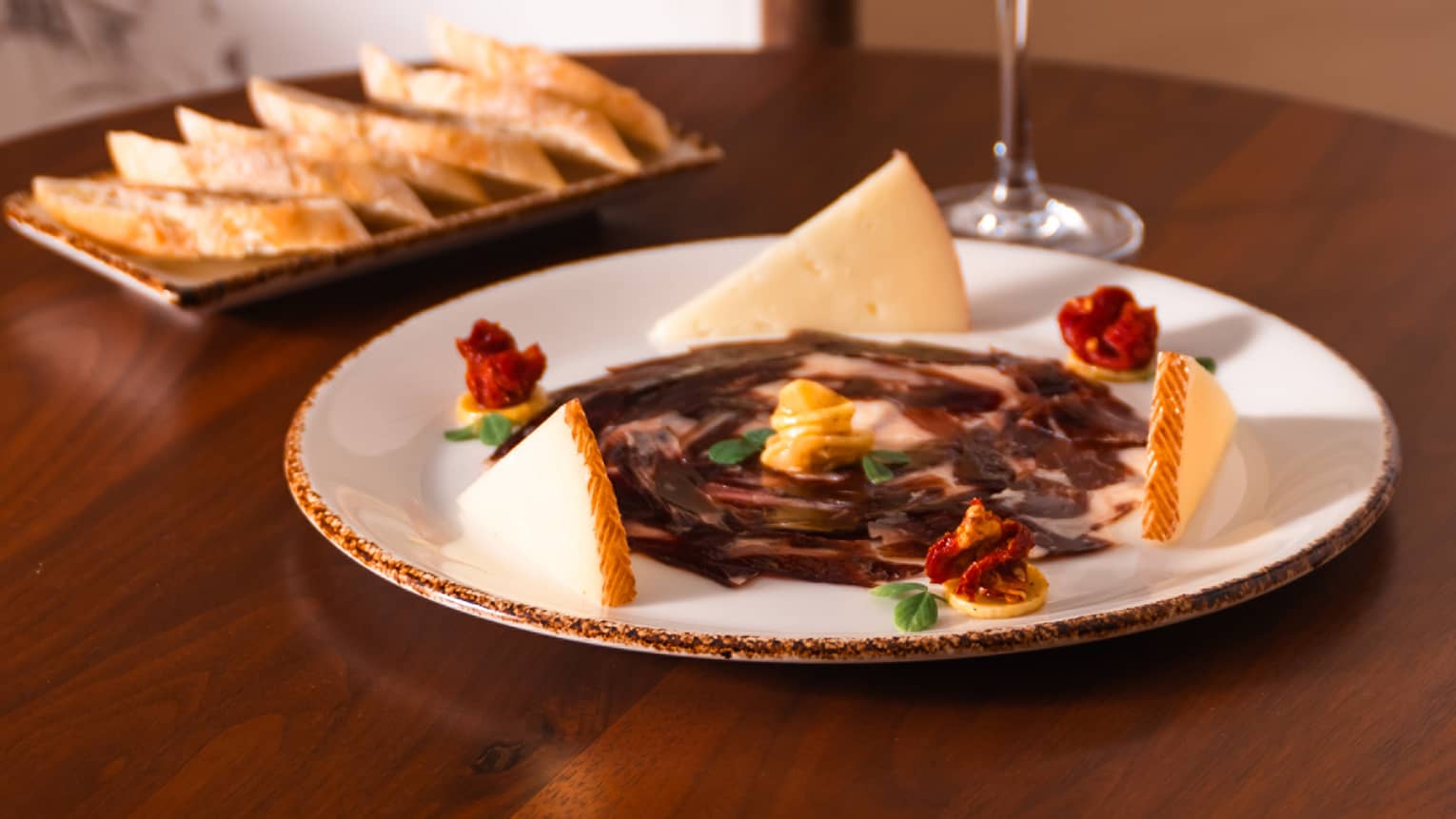 Meat and cheese on a plate with a glass of red wine.
