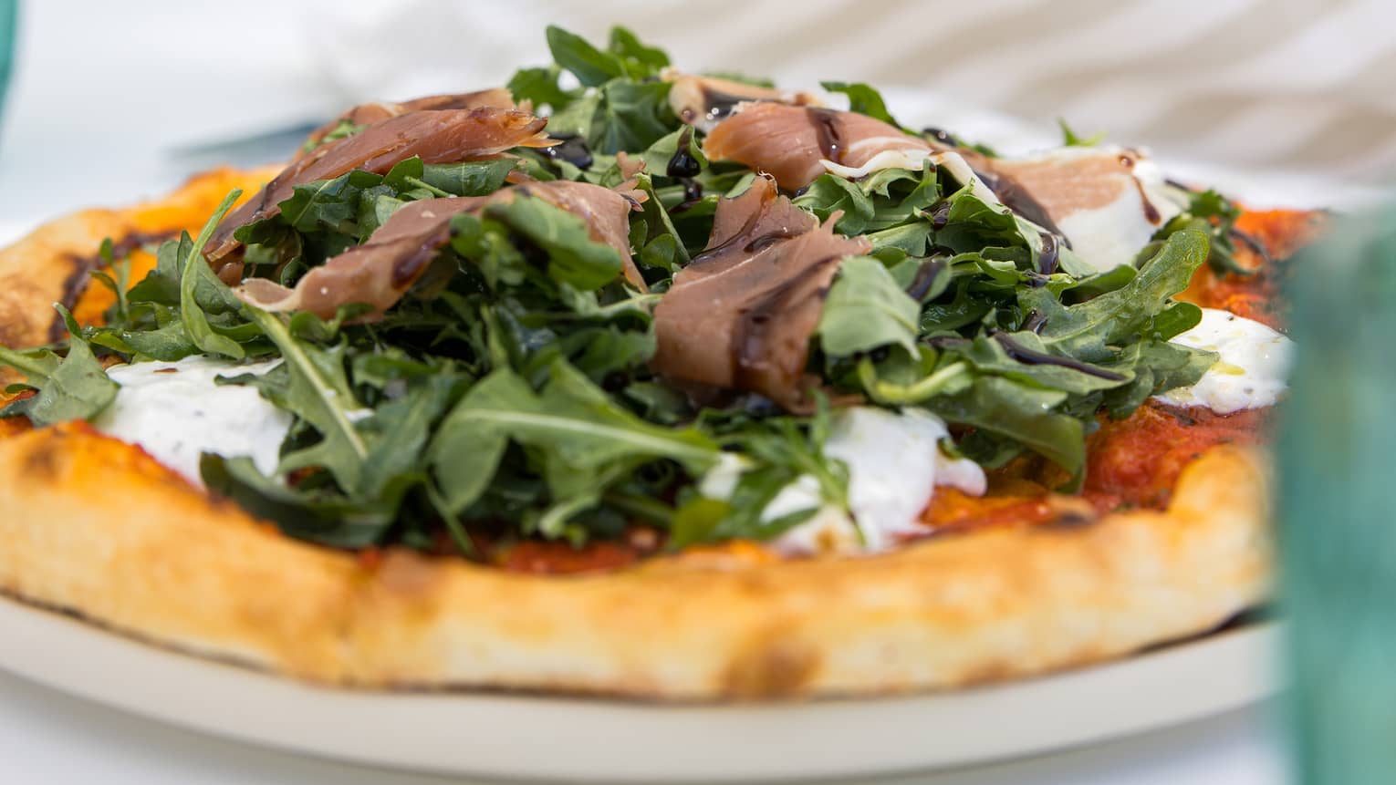 Pizza topped with prosciutto crudo, creamy burrata and fresh arugula