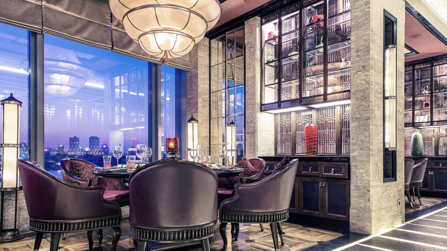 Dining table with black leather and purple velvet bucket-style chairs under tiered, cone-shaped chandelier 