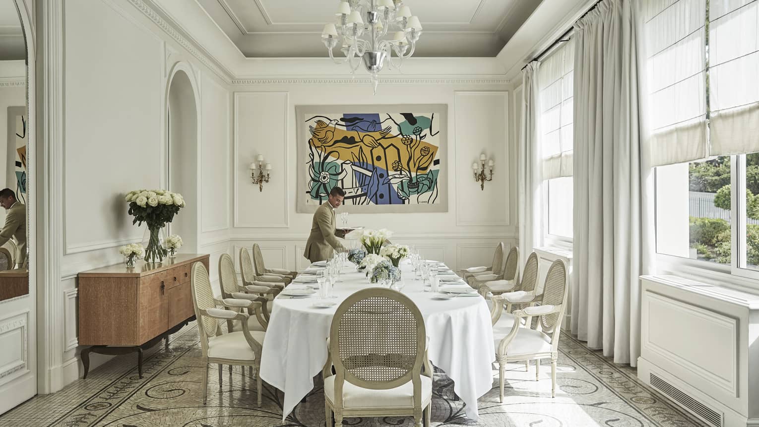 Server sets table in bright Salon les pins event space with modern art, tile floors, large windows